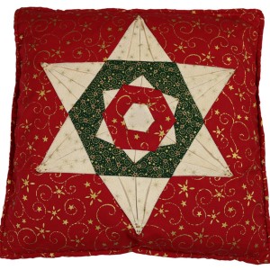 The folded star cushion cover. The main colour is red which forms the bacground. the start is formed using a cream colour and the detail is picked out in green and red. Gold details appear on the fabric.