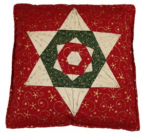 A brightly coloured Christmas cushion with a star pattern.  The main colour is red  and forms the background.  The details are picked out in cream, gold, green and red.